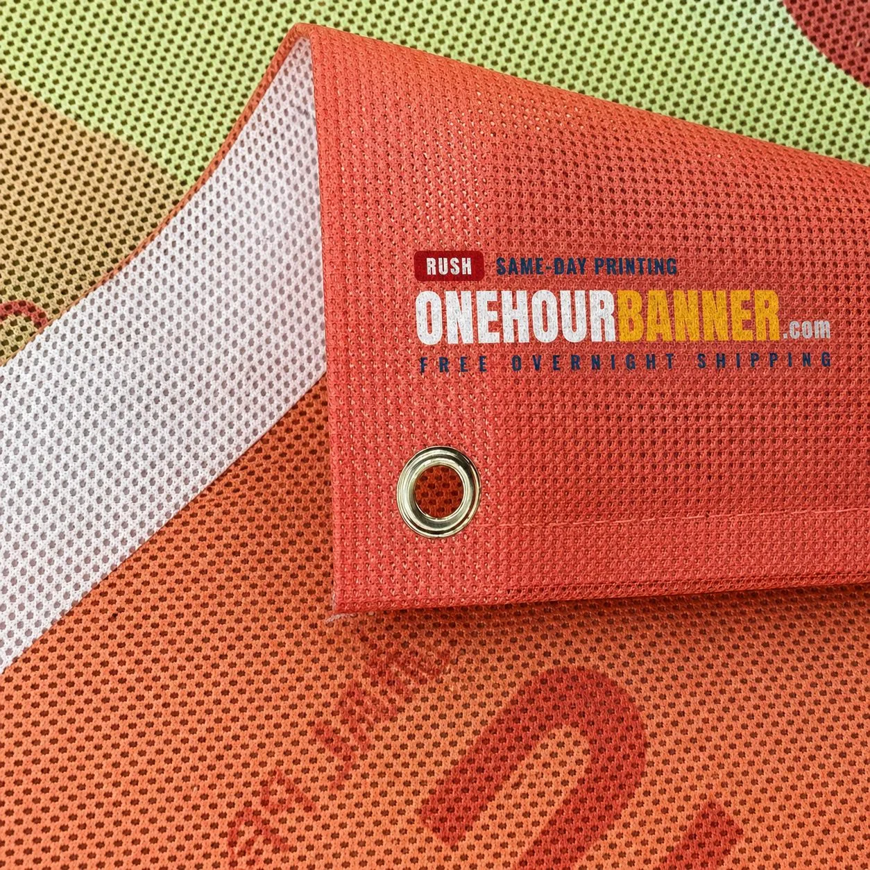 Custom mesh banner material close-up showing ONEHOURBANNER.com logo and brass grommets